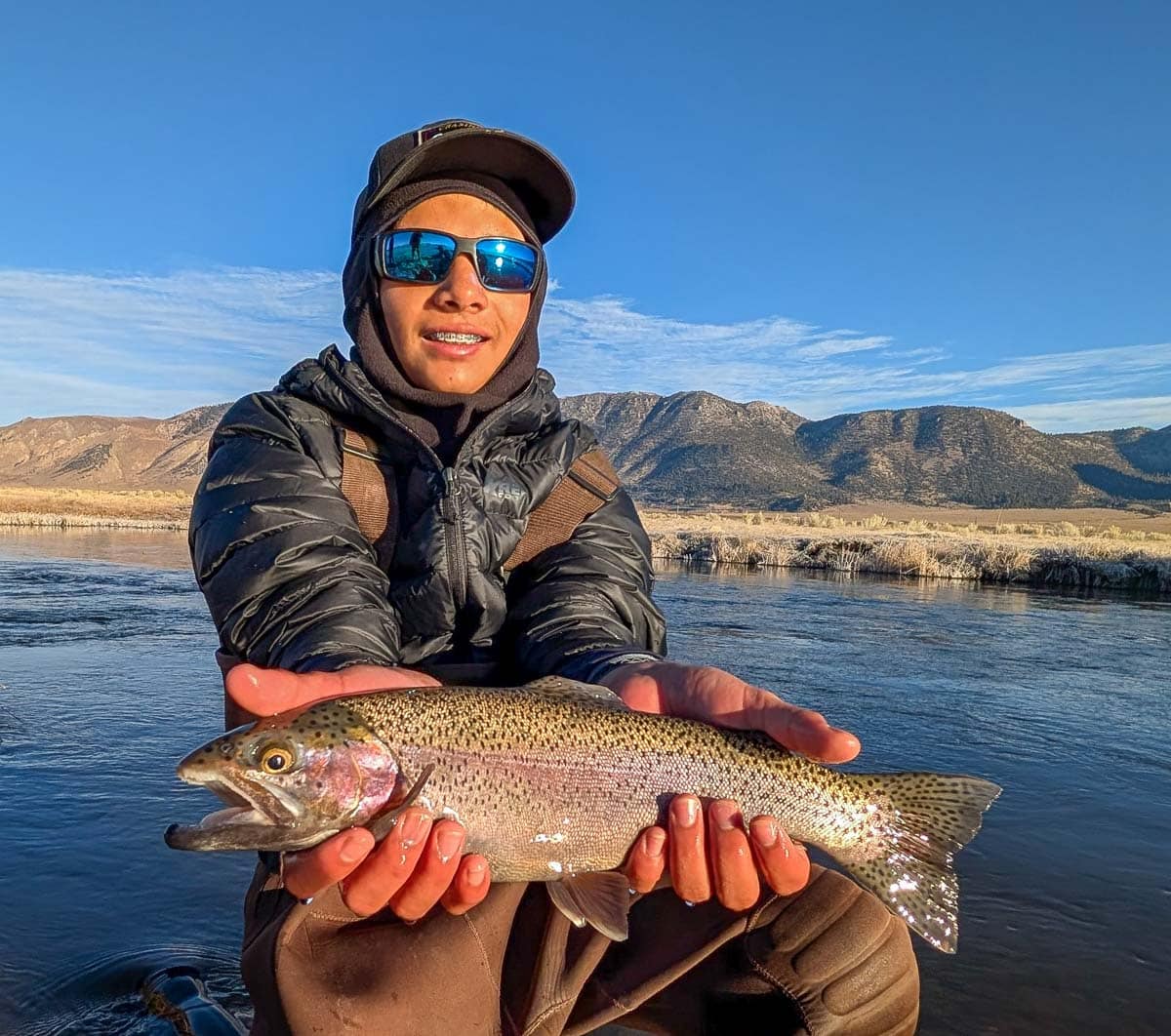 A smiling fly fisherman holding a larger rainbow trout on the Upper Owens River near Mammoth Lakes, CA.