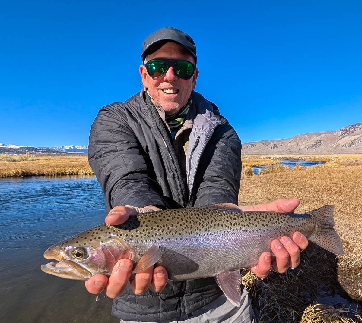 A smiling fly fisherman holding a larger rainbow trout on the Upper Owens River near Mammoth Lakes, CA.