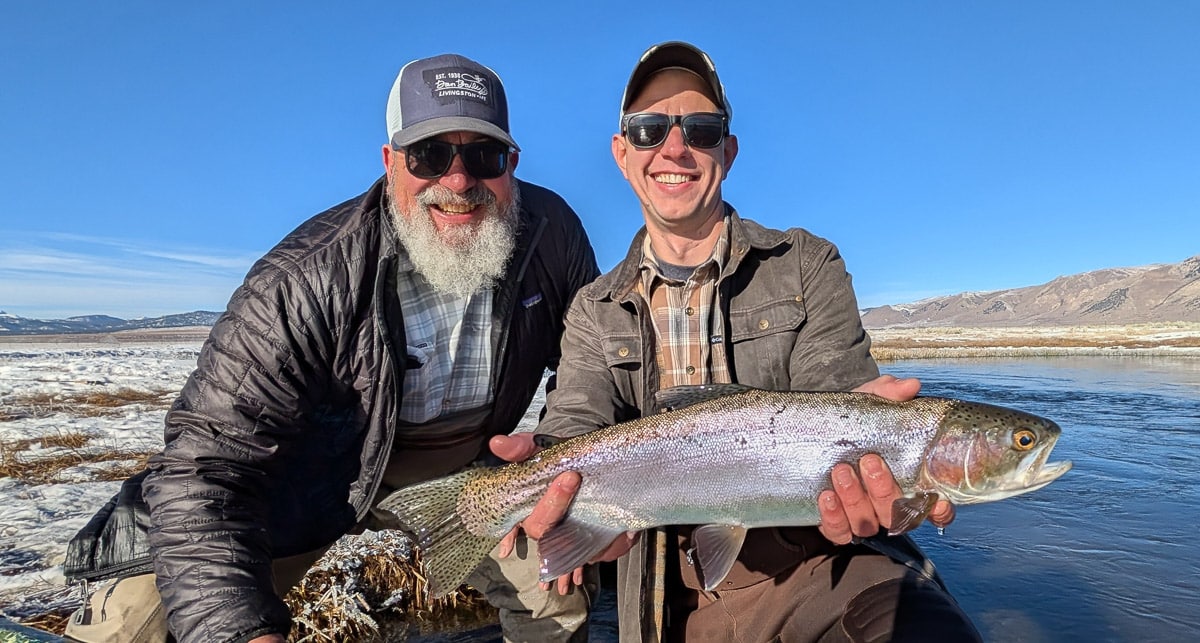 A smiling fly fisherman holding a larger rainbow trout on the Upper Owens River near Mammoth Lakes, CA.