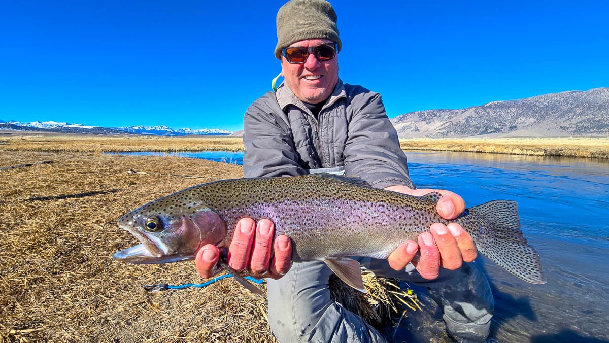 A smiling fly fisherman holding a larger rainbow trout on the Upper Owens River near Mammoth Lakes, CA.