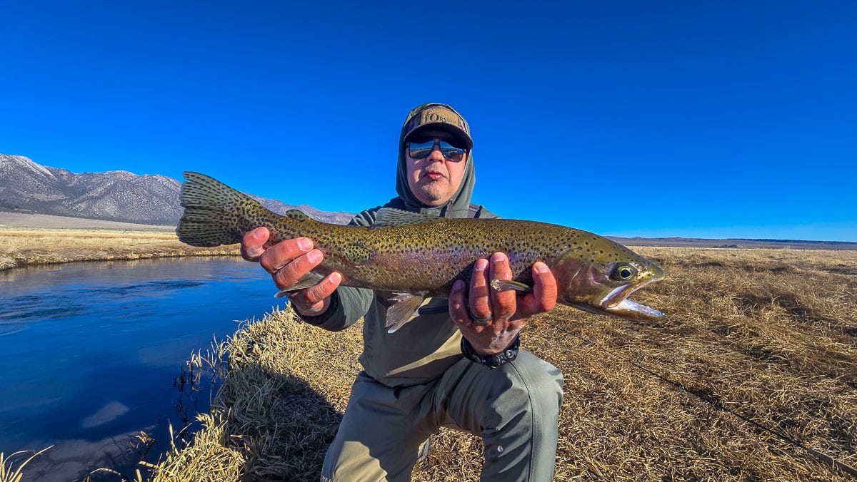 A smiling fly fisherman holding a larger rainbow trout on the Upper Owens River near Mammoth Lakes, CA.