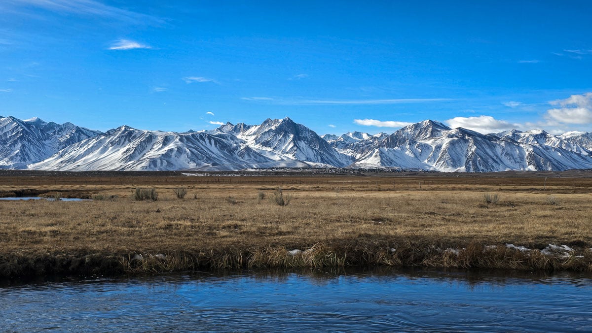 Snow filled mountains and a river flowing through a grassy meadow near Mammoth Lakes, CA