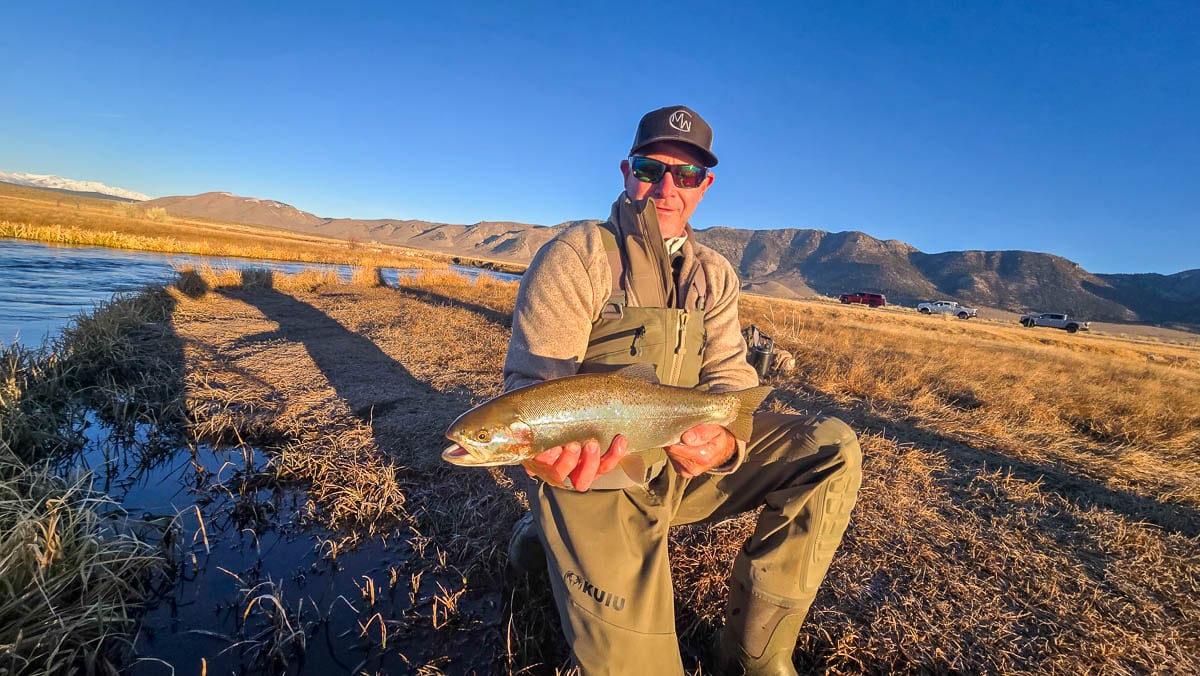 A smiling fly fisherman holding a larger rainbow trout on the Upper Owens River near Mammoth Lakes, CA.