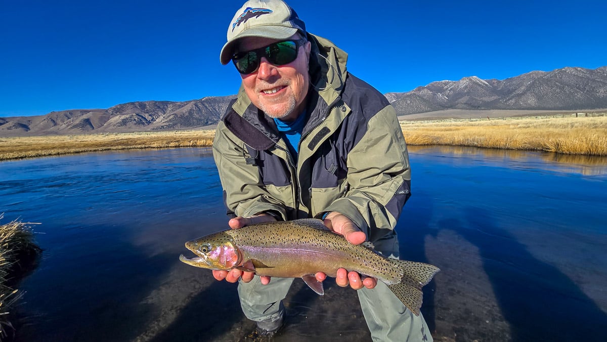 A smiling fly fisherman holding a larger rainbow trout on the Upper Owens River near Mammoth Lakes, CA.