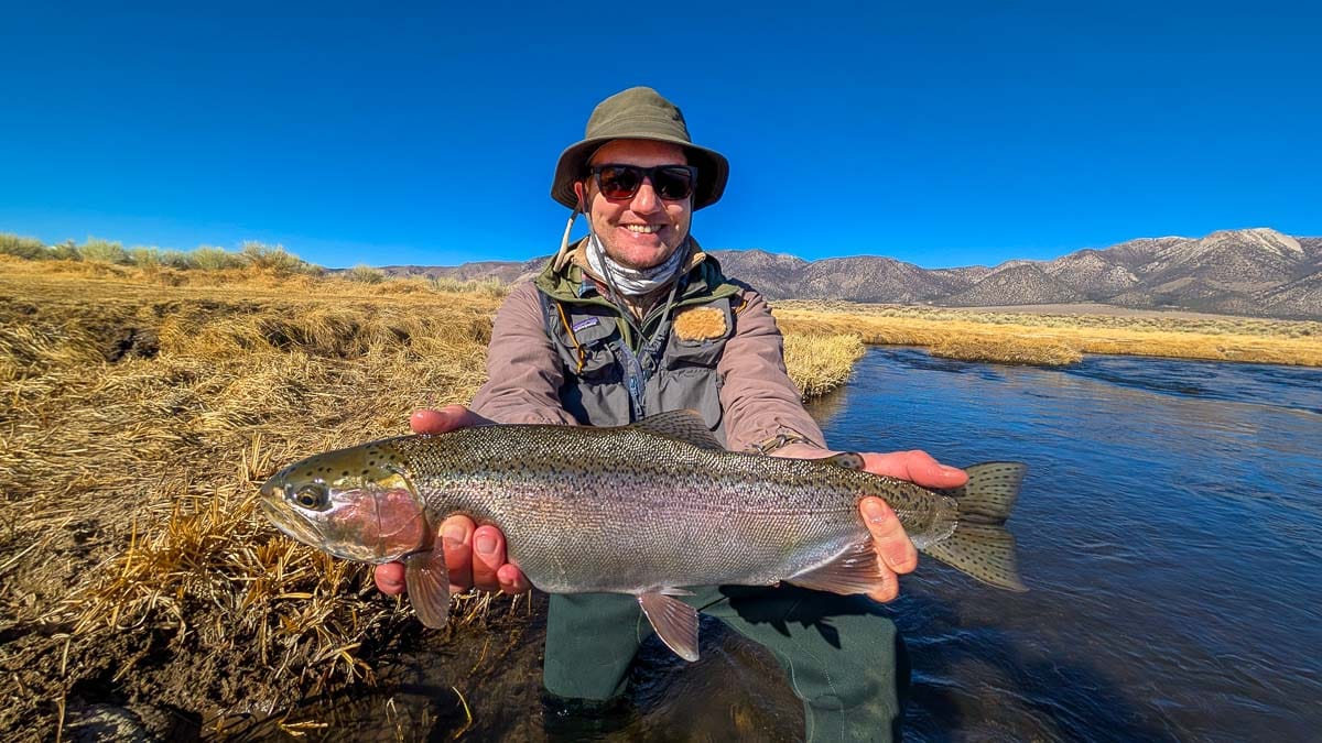 A smiling fly fisherman holding a larger rainbow trout on the Upper Owens River near Mammoth Lakes, CA.