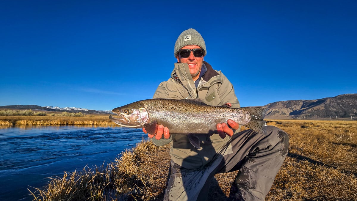 A smiling fly fishermen holding a giant rainbow trout on the Upper Owens River near Mammoth Lakes, CA