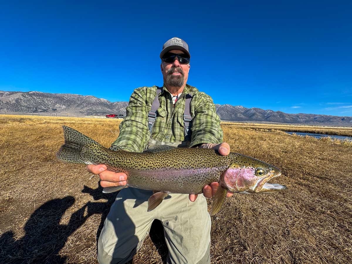 A smiling fly fisherman holding a larger rainbow trout on the Upper Owens River near Mammoth Lakes, CA.