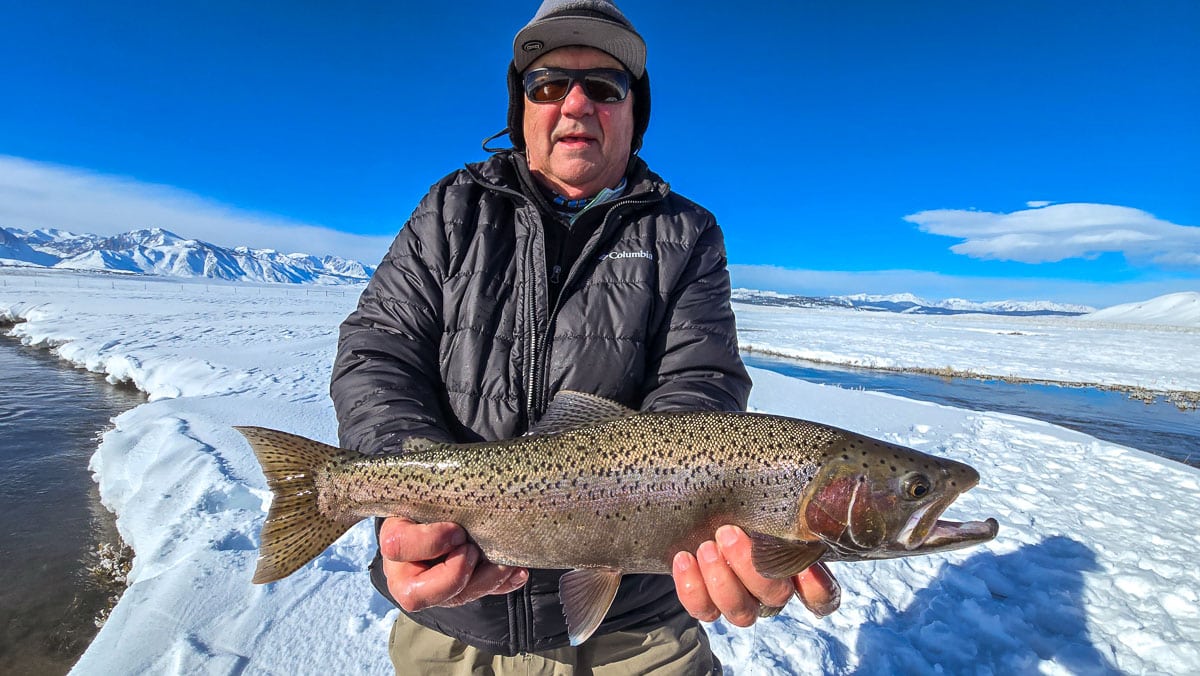 A smiling fly fisherman holding a larger rainbow trout on the Upper Owens River near Mammoth Lakes, CA.