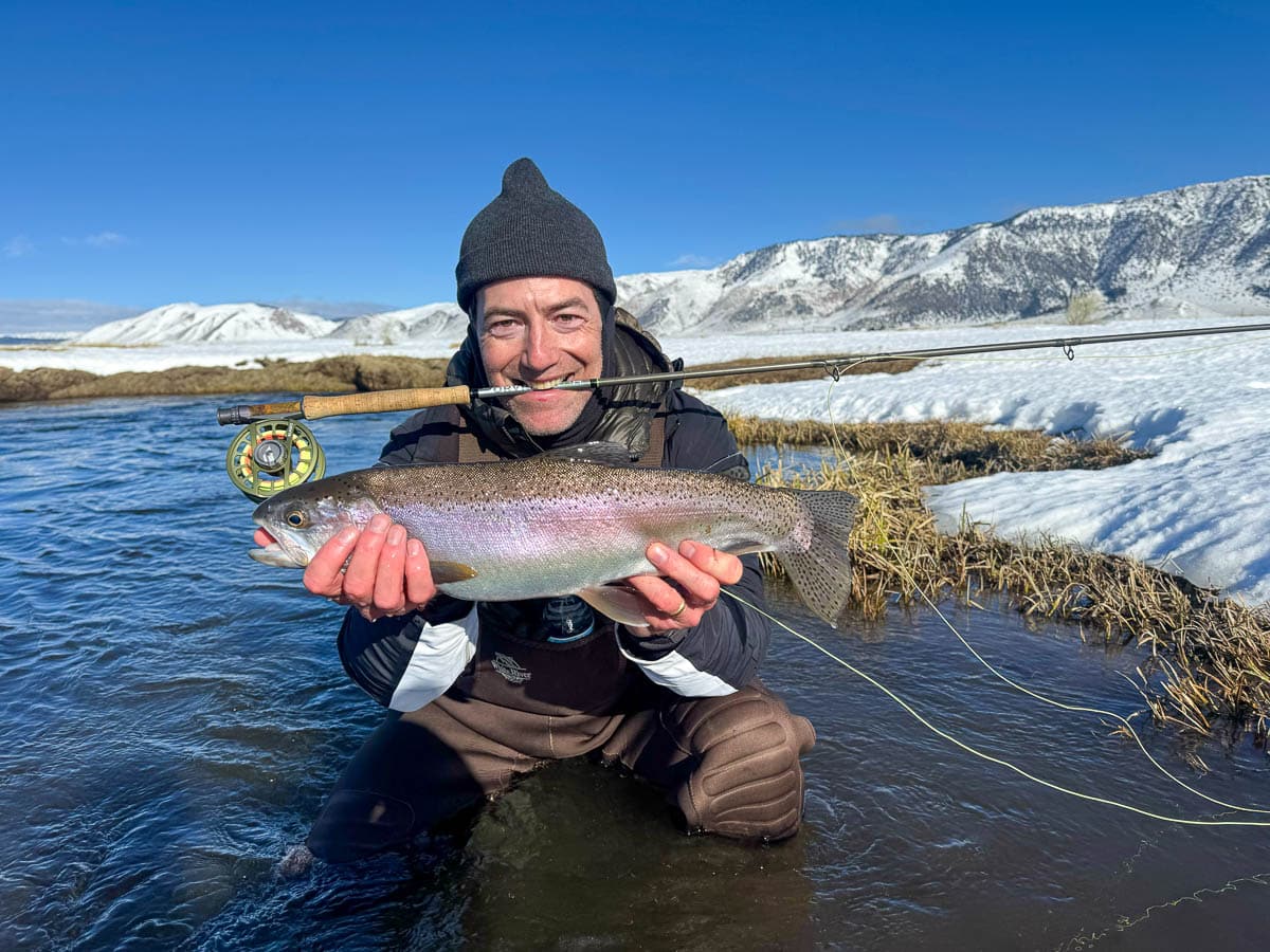 A smiling fly fisherman holding a larger rainbow trout on the Upper Owens River near Mammoth Lakes, CA.