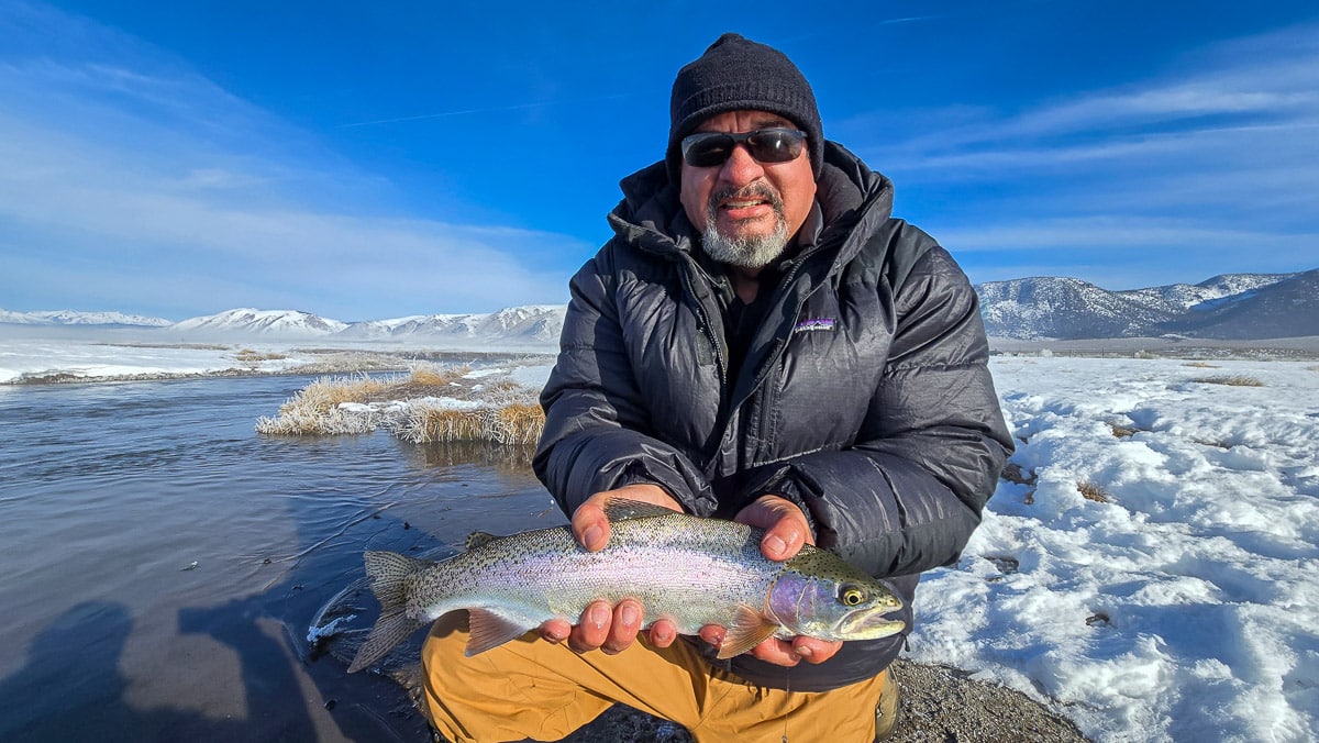 A smiling fly fisherman holding a larger rainbow trout on the Upper Owens River near Mammoth Lakes, CA.