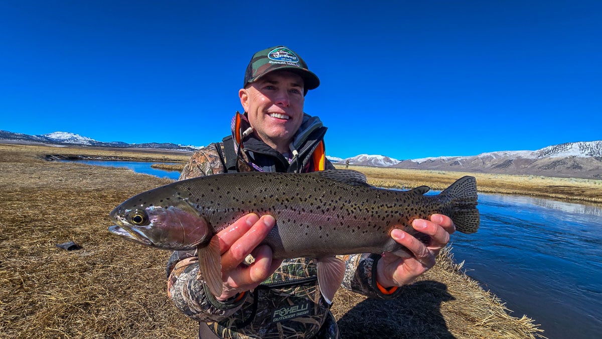 A smiling fly fisherman holding a larger rainbow trout on the Upper Owens River near Mammoth Lakes, CA.