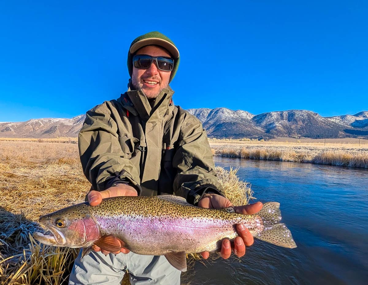 A smiling fly fisherman holding a larger rainbow trout on the Upper Owens River near Mammoth Lakes, CA.