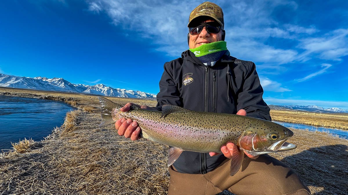 A smiling fly fisherman holding a larger rainbow trout on the Upper Owens River near Mammoth Lakes, CA.