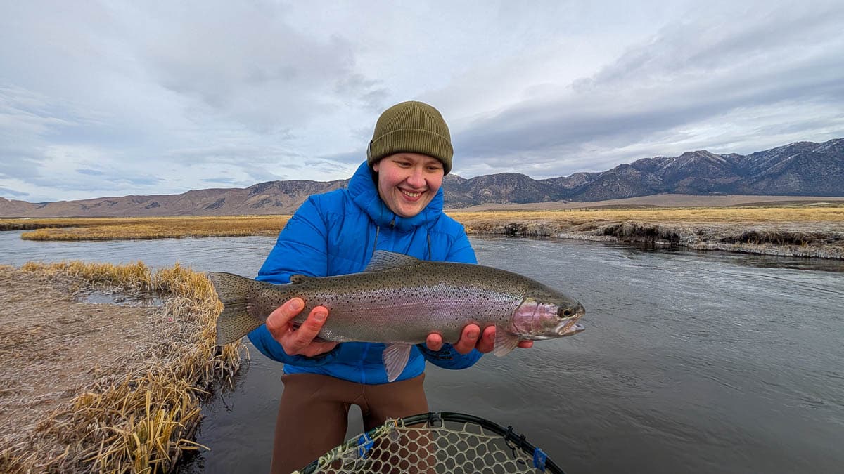 A smiling fly fishermen holding a giant rainbow trout on the Upper Owens River near Mammoth Lakes, CA