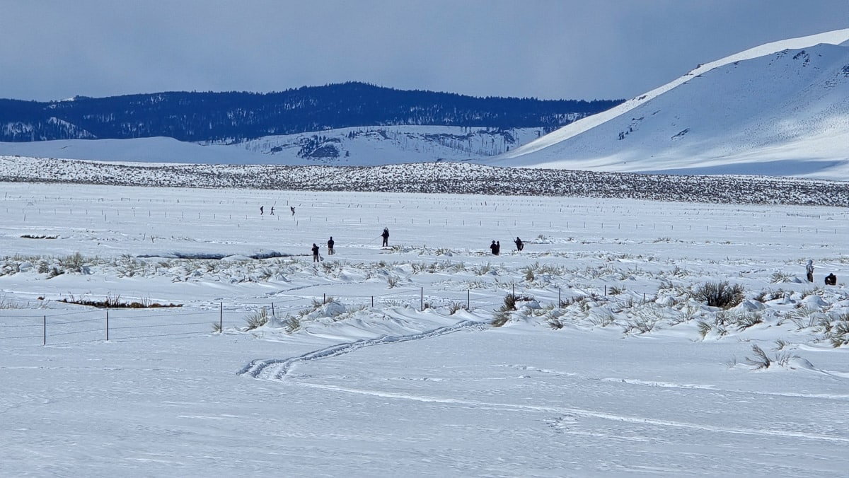 A snow filled pasture with a number of people fishing on the Upper Owens River near Mammoth Lakes, CA