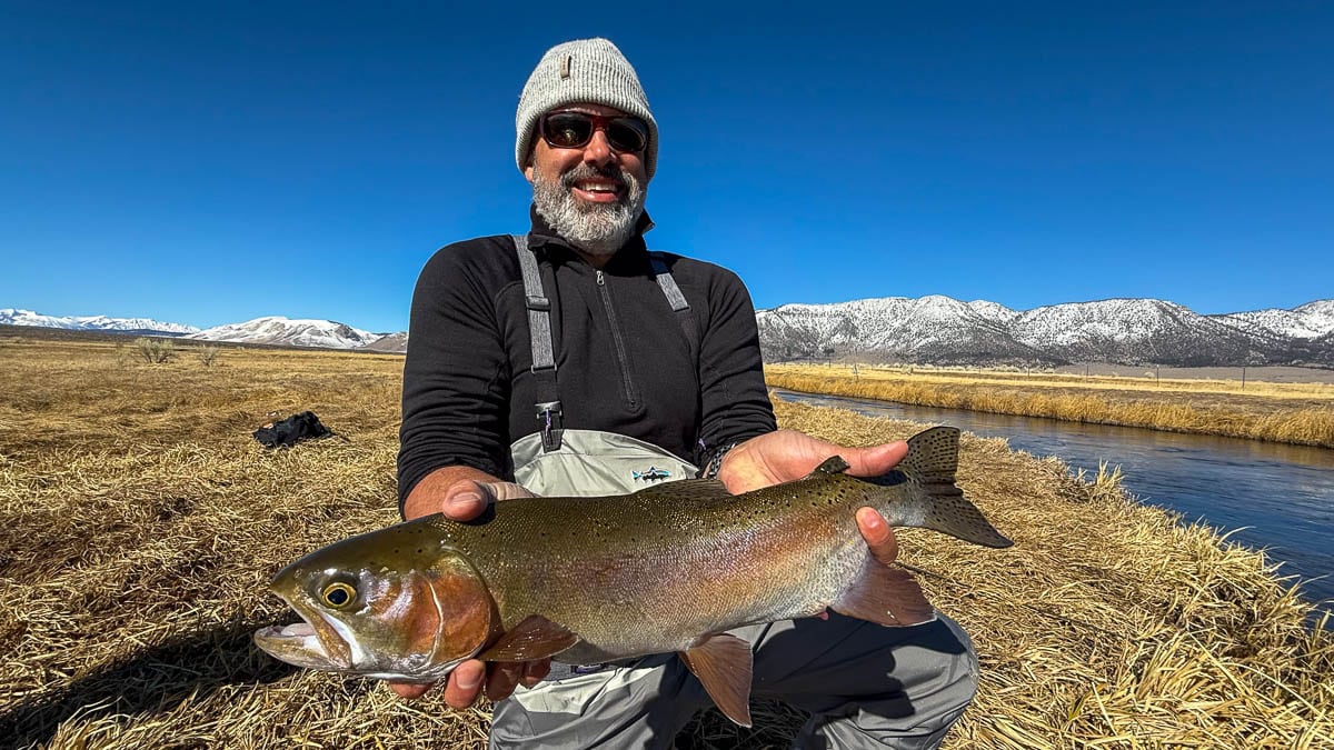 A smiling fly fisherman holding a larger rainbow trout on the Upper Owens River near Mammoth Lakes, CA.