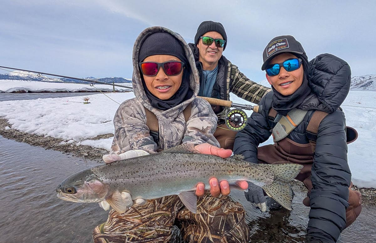 A smiling fly fisherman holding a larger rainbow trout on the Upper Owens River near Mammoth Lakes, CA.