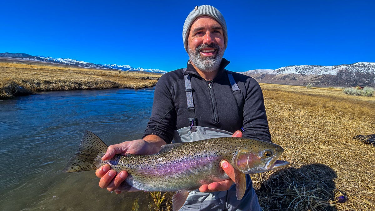 A smiling fly fisherman holding a larger rainbow trout on the Upper Owens River near Mammoth Lakes, CA.