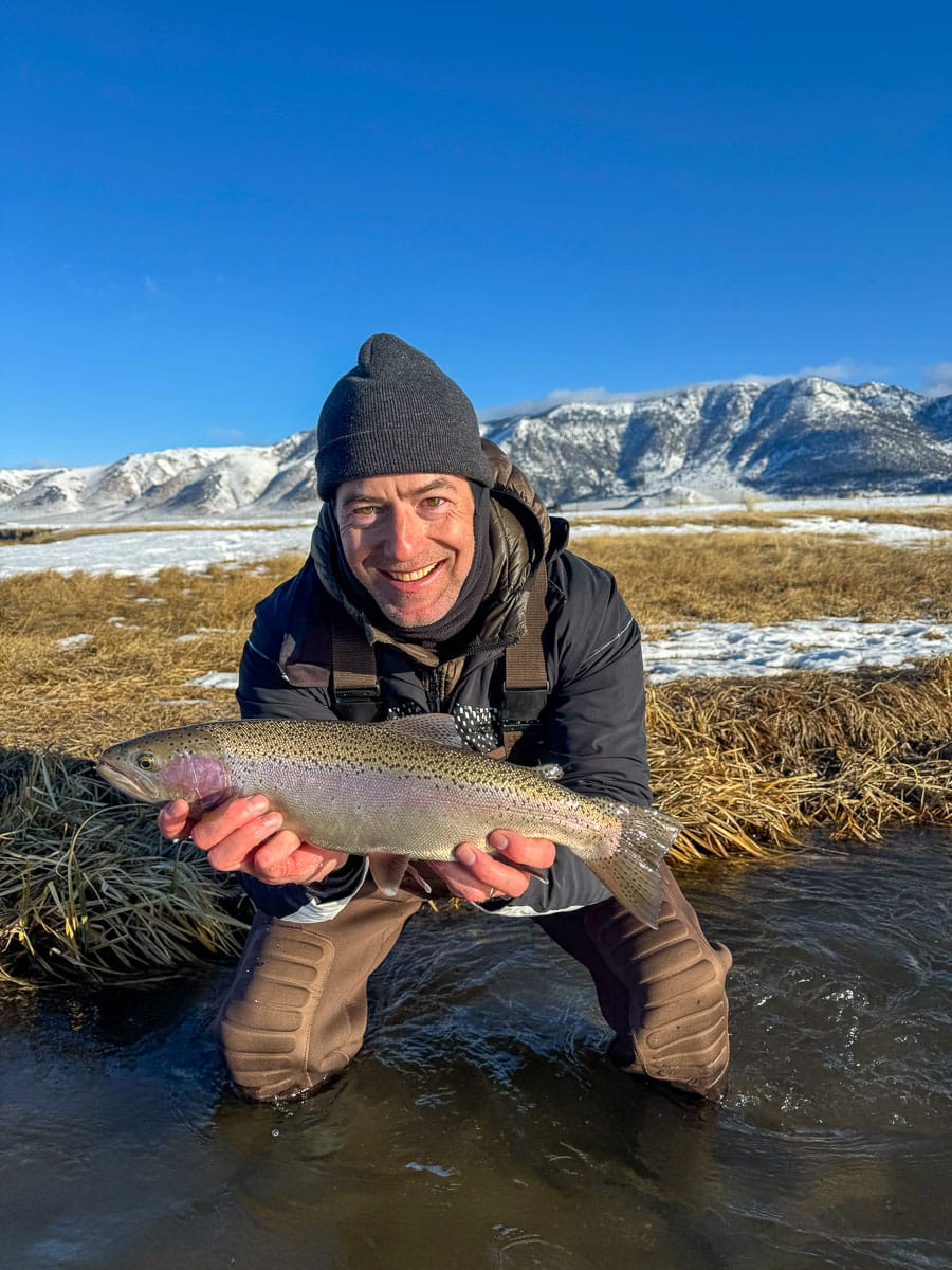 A smiling fly fisherman holding a larger rainbow trout on the Upper Owens River near Mammoth Lakes, CA.