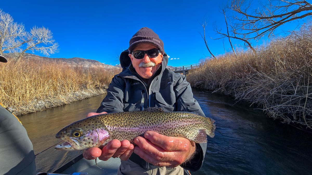 A fly fisherman holding a rainbow trout on the Lower Owens River.