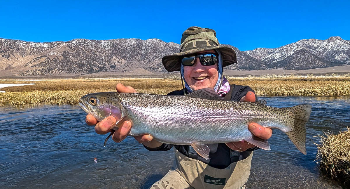 A smiling fly fisherman holding a larger rainbow trout on the Upper Owens River near Mammoth Lakes, CA.