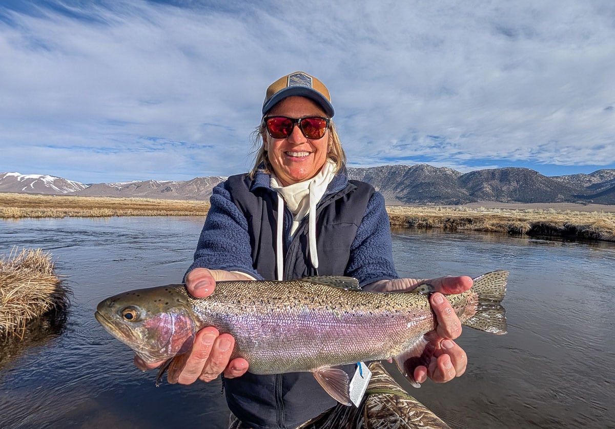 A smiling fly fisherman holding a larger rainbow trout on the Upper Owens River near Mammoth Lakes, CA.