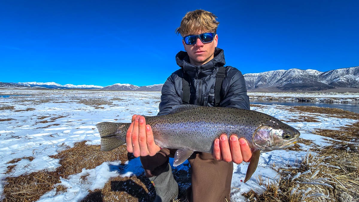 A smiling fly fisherman holding a larger rainbow trout on the Upper Owens River near Mammoth Lakes, CA.