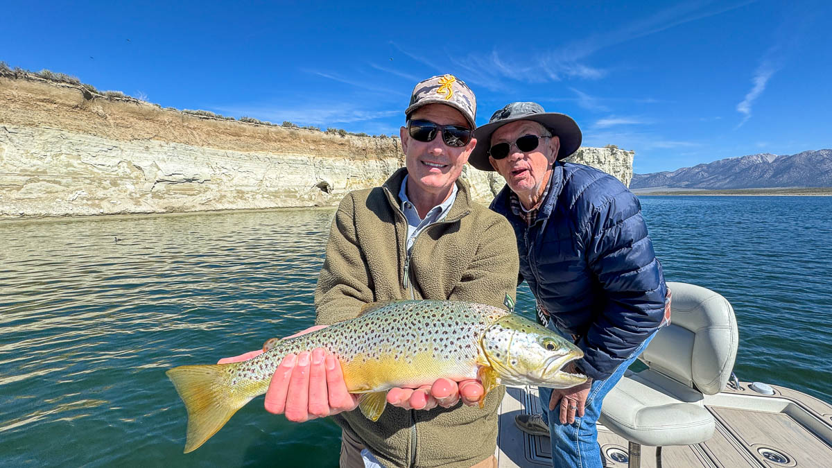 A smiling fly fisherman holding a large brown trout on the Crowley Lake near Mammoth Lakes, CA.