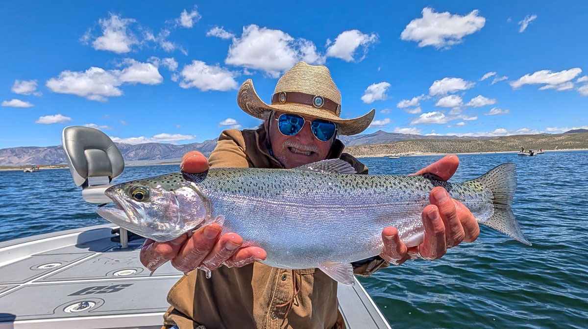A fly fisherman holding a large rainbow trout on Crowley Lake near Mammoth Lakes, CA