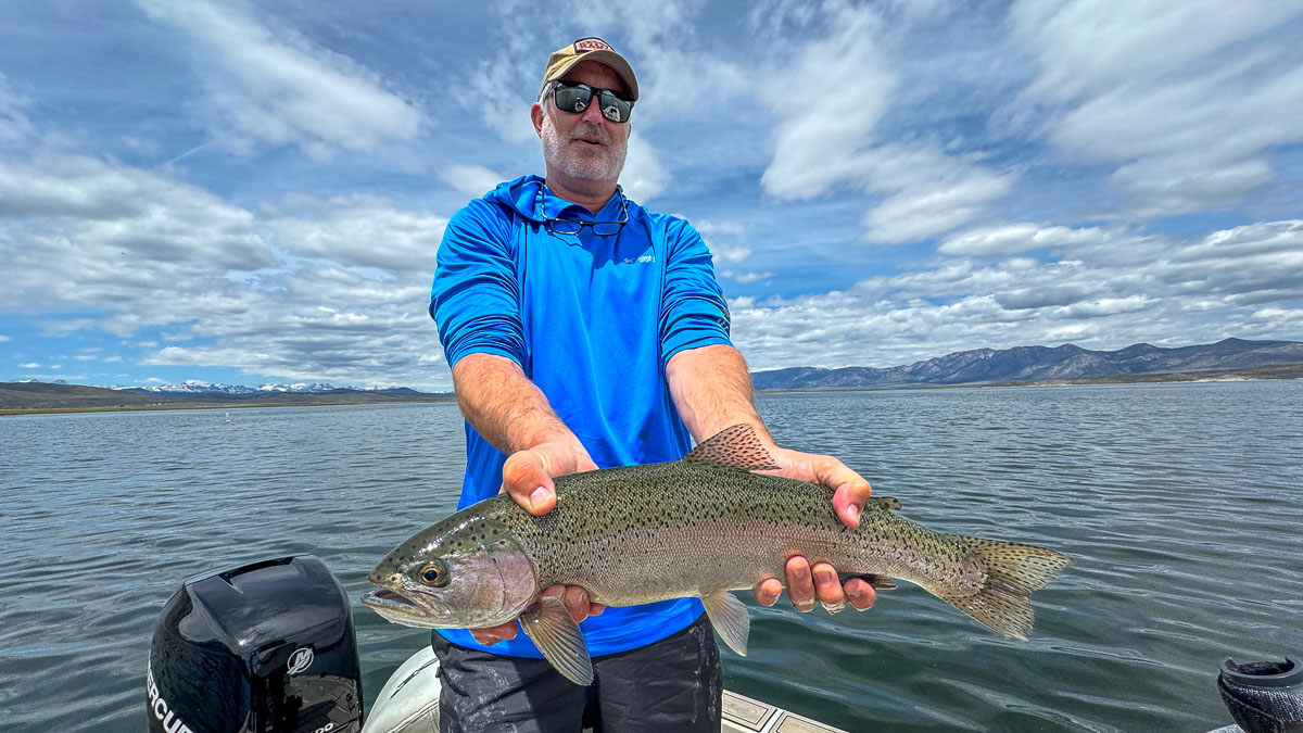 A fly fisherman holding a large rainbow trout on Crowley Lake near Mammoth Lakes, CA