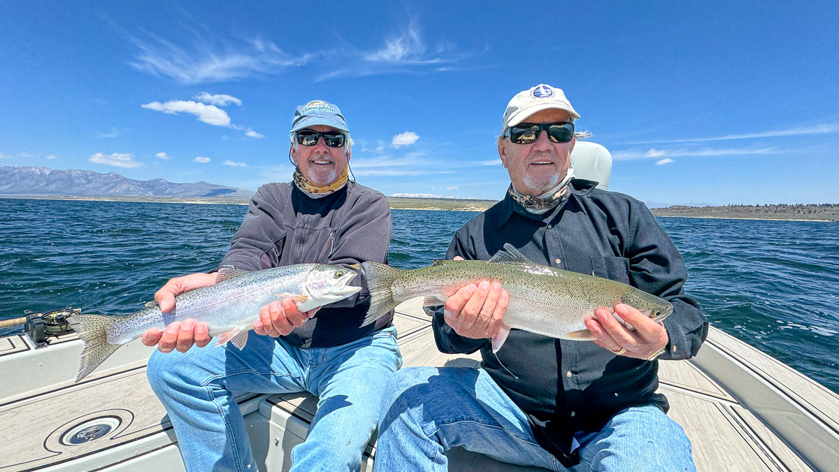 A couple of fly fishermen holding a pair of large rainbow trout on Crowley Lake in a boat.