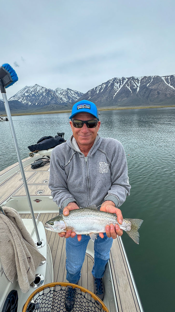 A fly fisherman holding a large rainbow trout on Crowley Lake near Mammoth Lakes, CA