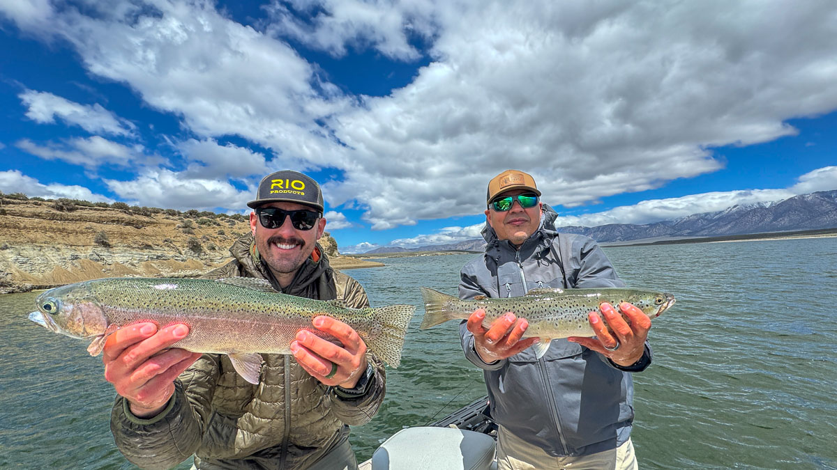 A couple of fly fishermen holding a rainbow and a brown trout on Crowley Lake in a boat near Mammoth Lakes, CA