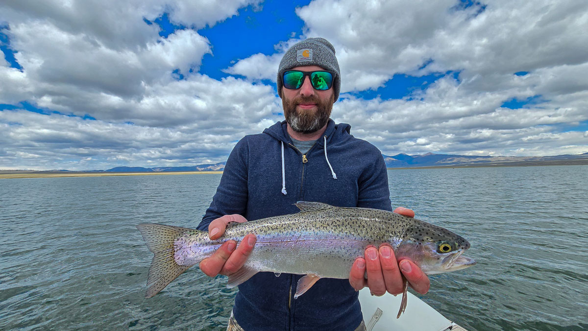 A smiling fly fisherman holding a large rainbow trout on the Crowley Lake near Mammoth Lakes, CA.