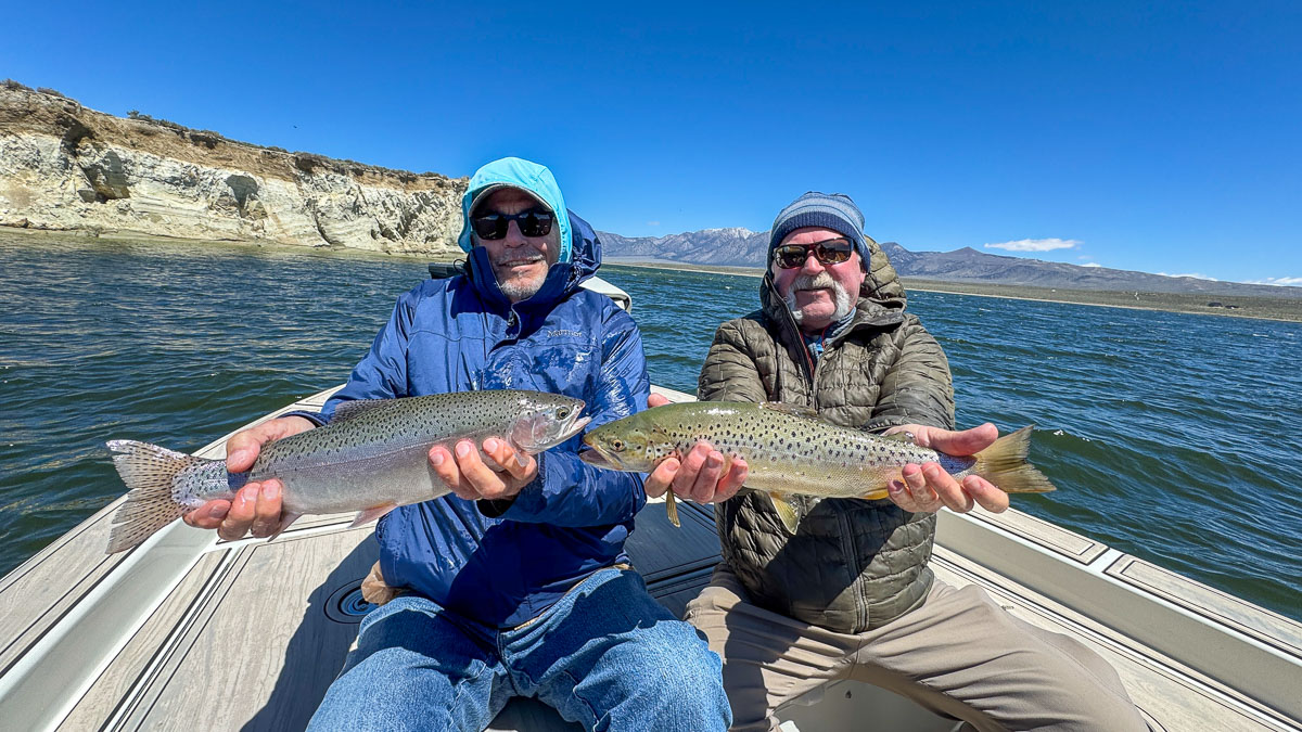 A couple of fly fishermen holding a rainbow and a brown trout on Crowley Lake in a boat near Mammoth Lakes, CA