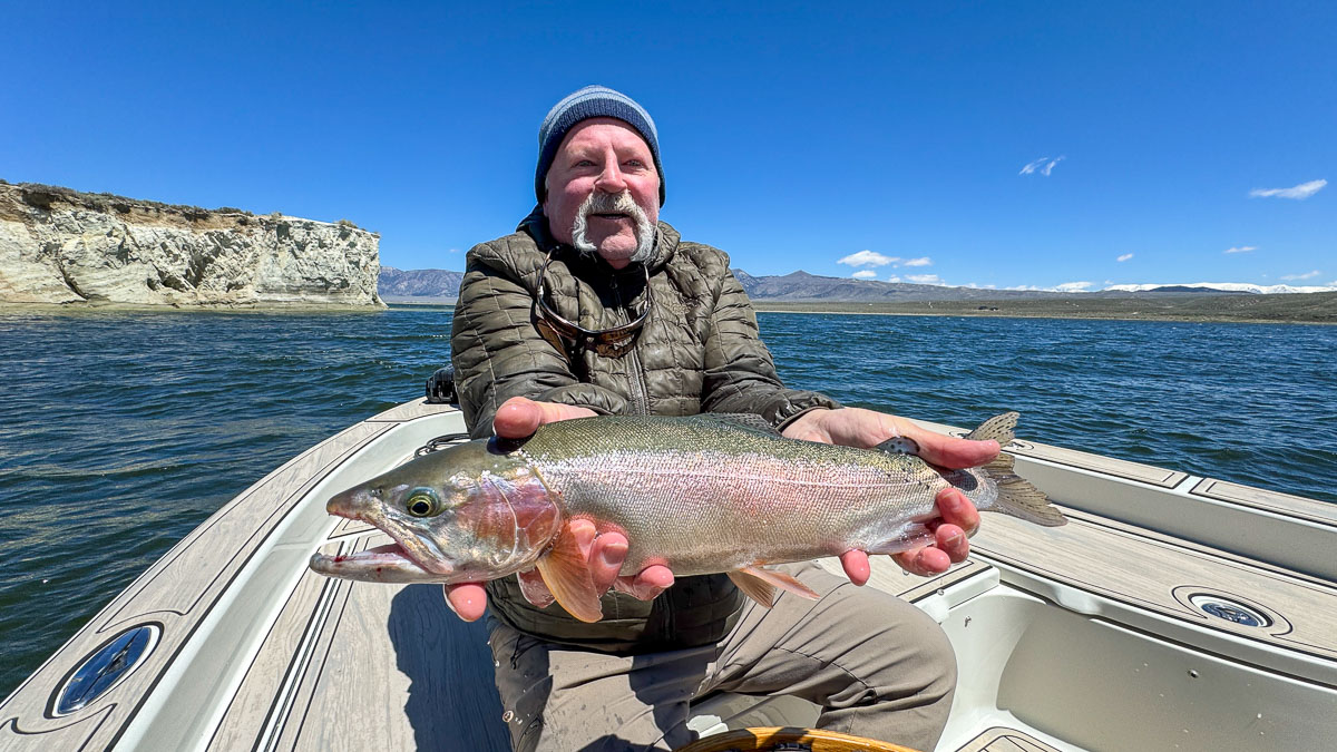 A fly fisherman holding a large rainbow trout on Crowley Lake near Mammoth Lakes, CA