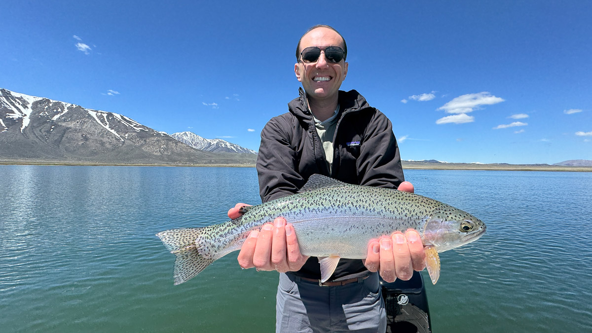 A fly fisherman holding a large rainbow trout on Crowley Lake near Mammoth Lakes, CA