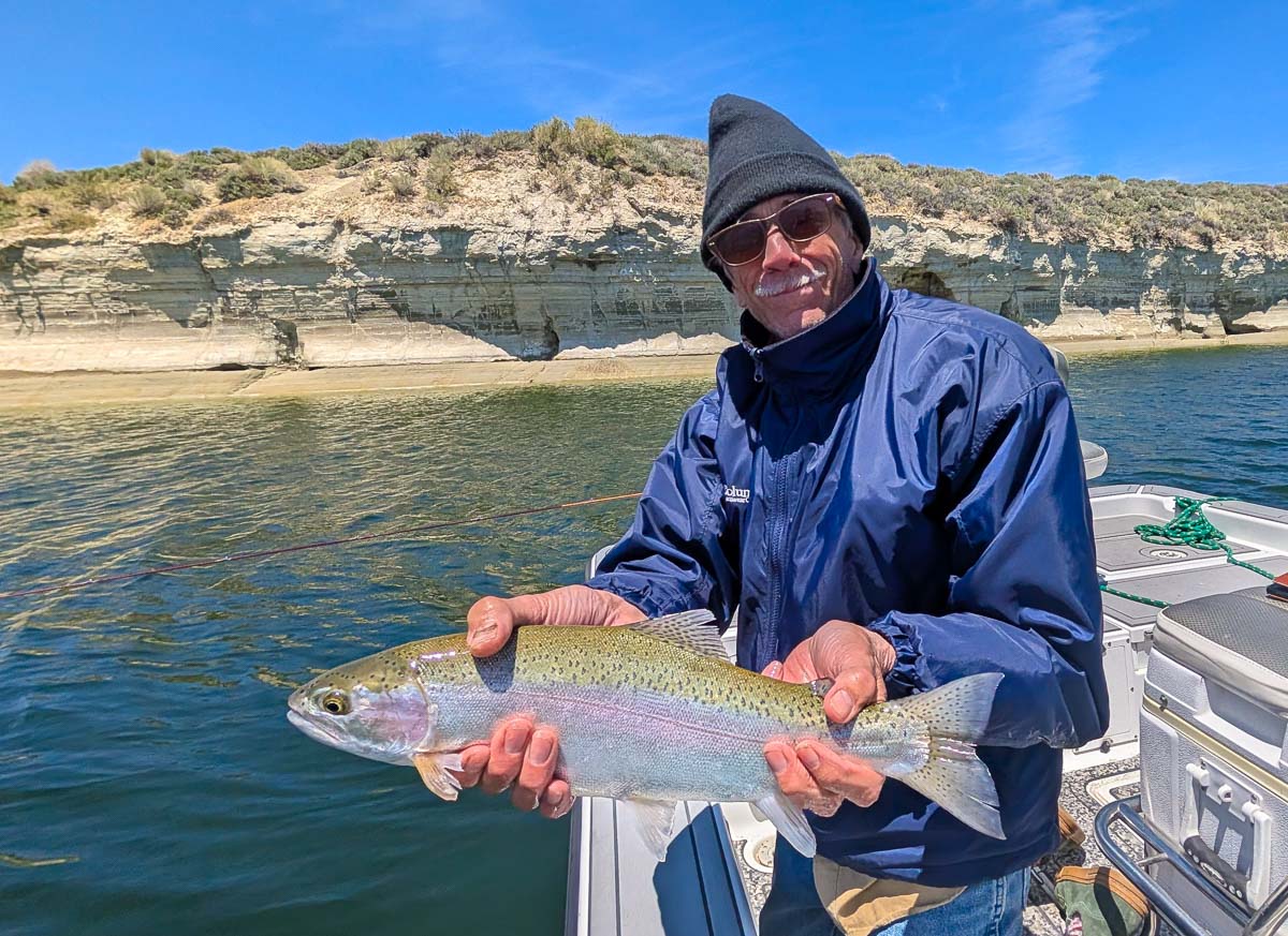 A fly fisherman holding a large rainbow trout on Crowley Lake near Mammoth Lakes, CA