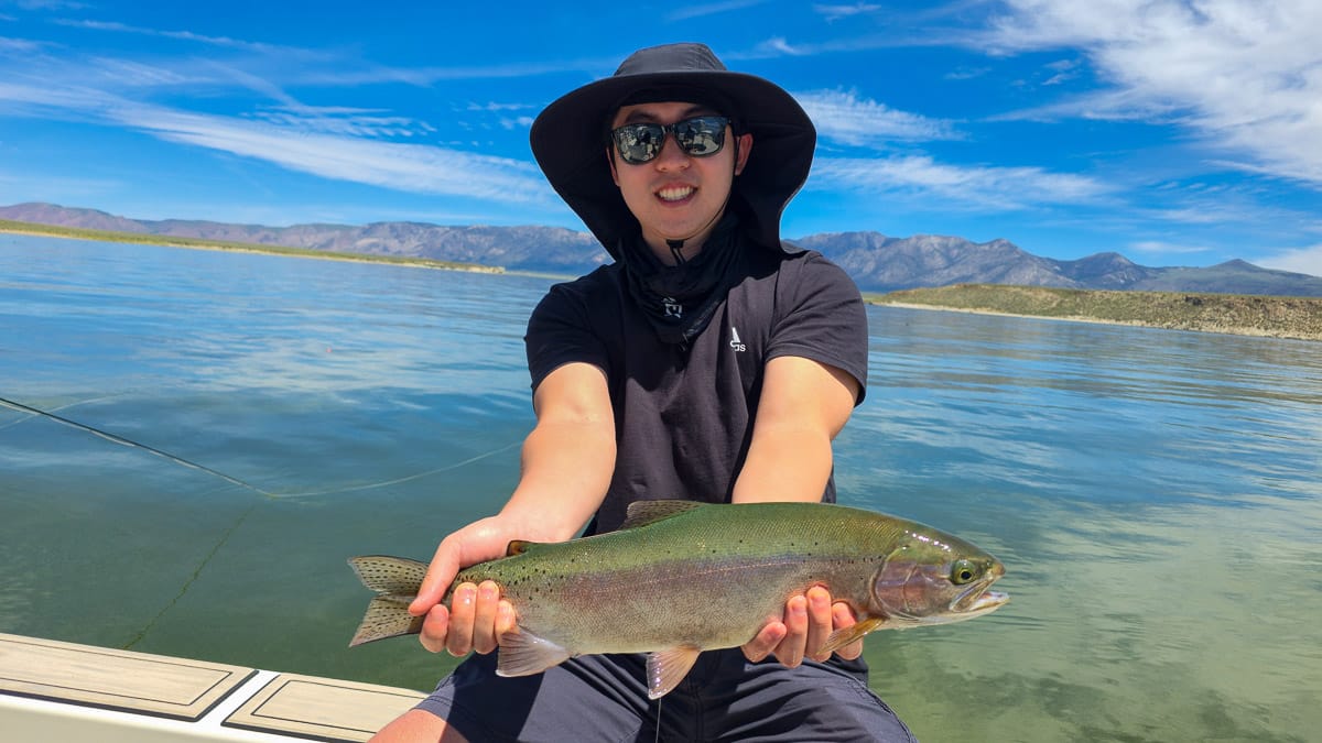 A smiling fly fisherman holding a large rainbow trout on the Crowley Lake near Mammoth Lakes, CA.