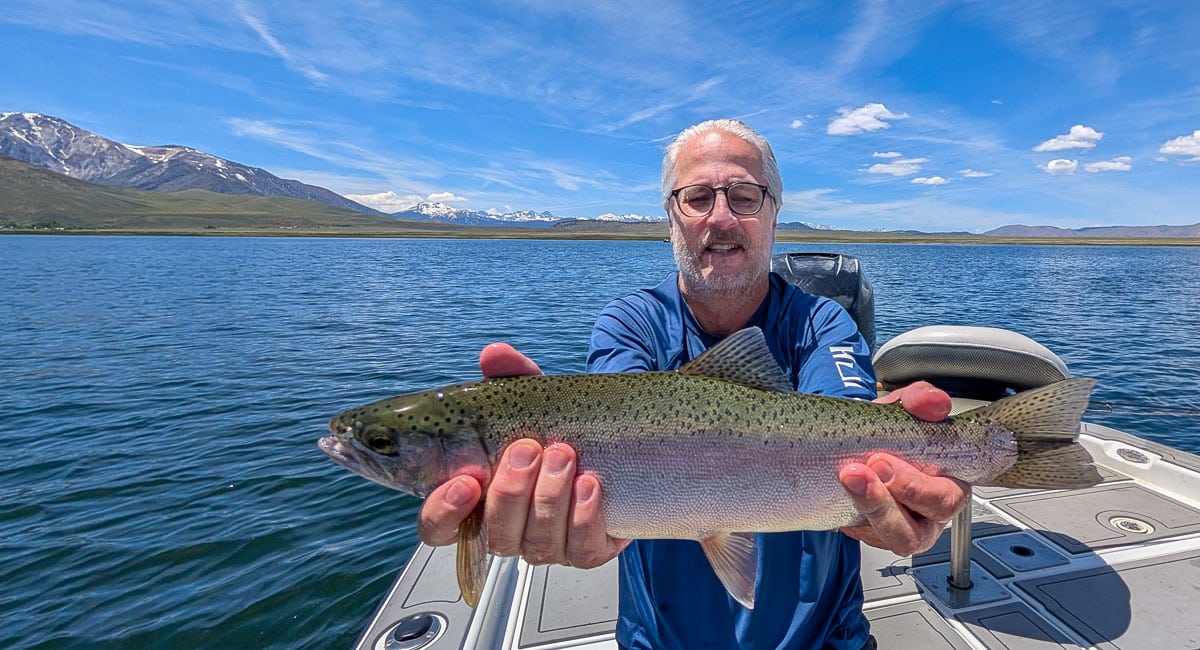 A fly fisherman holding a large rainbow trout on Crowley Lake near Mammoth Lakes, CA