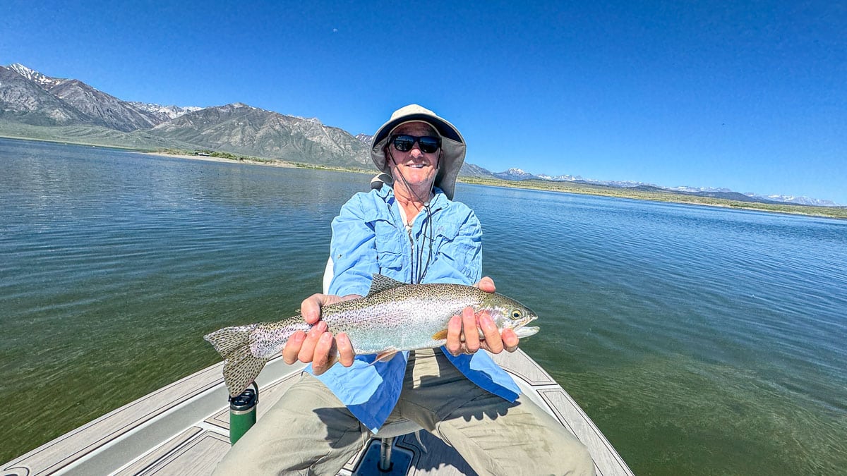 A fly fisherman holding a large rainbow trout on Crowley Lake near Mammoth Lakes, CA