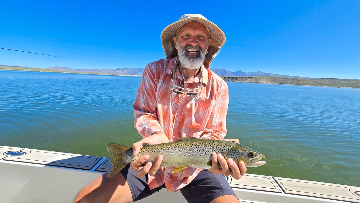 A fly fisherman holding a large brown trout on Crowley Lake near Mammoth Lakes, CA