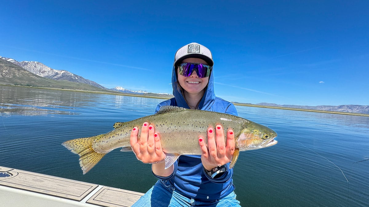 A smiling fly fisherman holding a large cutthroat trout on the Crowley Lake near Mammoth Lakes, CA.