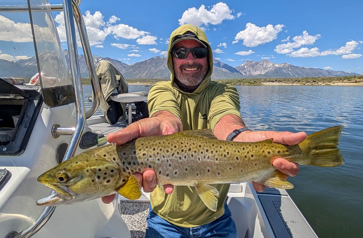 A fly fisherman holding a large brown trout on Crowley Lake near Mammoth Lakes, CA