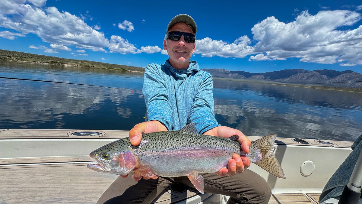 A fly fisherman holding a large rainbow trout on Crowley Lake near Mammoth Lakes, CA