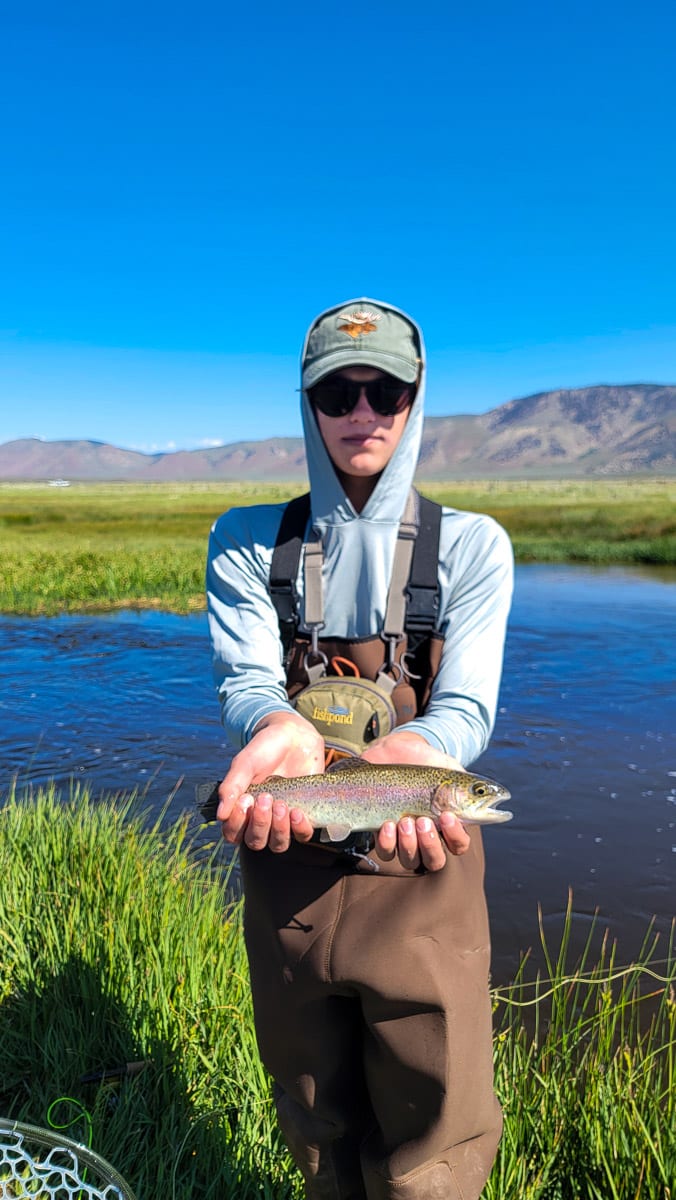 A fly fisherman holding a rainbow trout on Upper Owens River near Mammoth Lakes, CA