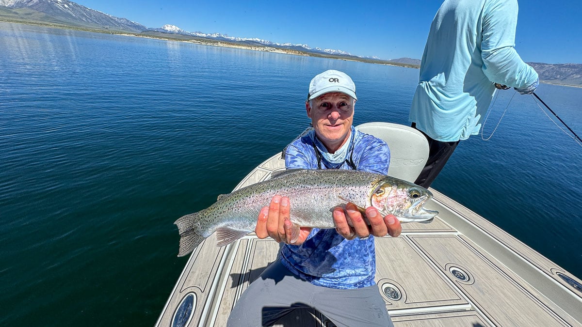 A fly fisherman holding a large rainbow trout on Crowley Lake near Mammoth Lakes, CA