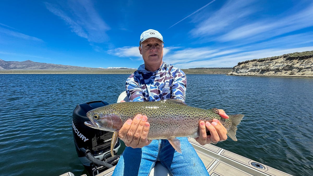 A fly fisherman holding a large rainbow trout on Crowley Lake near Mammoth Lakes, CA