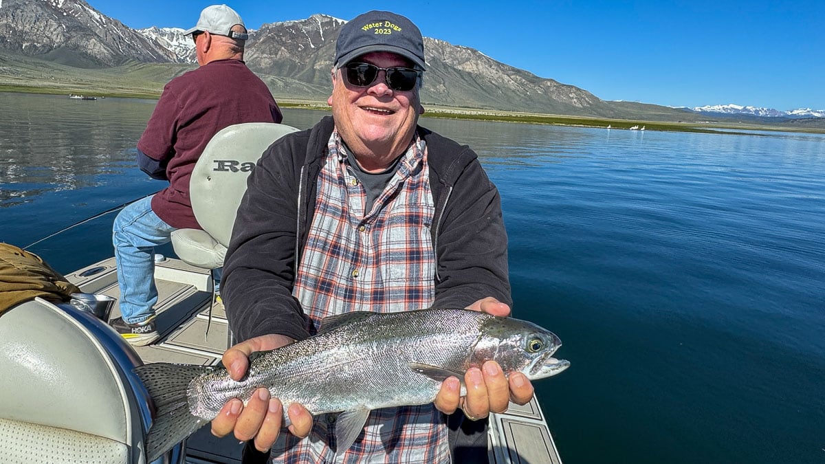 A fly fisherman holding a large rainbow trout on Crowley Lake near Mammoth Lakes, CA
