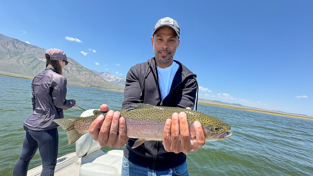 A smiling fly fisherman holding a large brown trout on the Crowley Lake near Mammoth Lakes, CA.